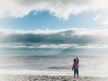 Rear view of man standing on beach against sky