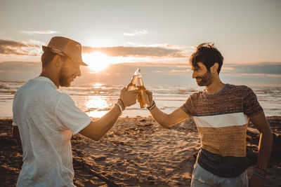 Friends on beach against sky during sunset