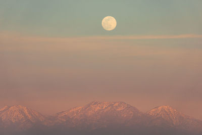Scenic view of full moon over snow capped mountain peak