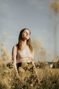 Young woman standing on field against sky