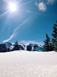 Snow covered landscape against sky on sunny day