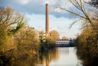 Smoke stack reflection in river amidst trees against sky