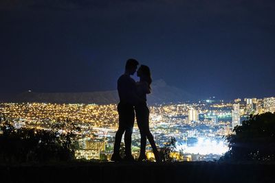 Silhouette couple against illuminated cityscape at night