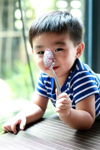 Portrait of cute baby boy holding spoon while lying by window at home