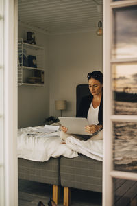 Mature woman using laptop while sitting on bed in holiday villa