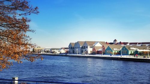 Buildings by river against blue sky