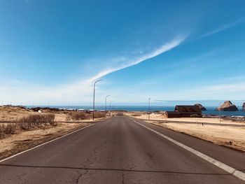 Empty road amidst land against blue sky