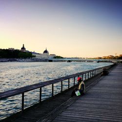 Pier over river against clear sky during sunset