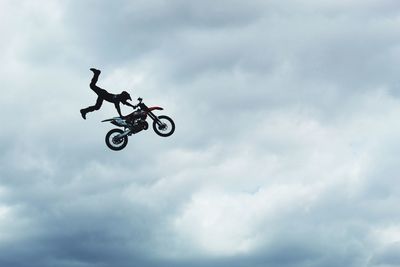 Low angle view of man performing stunt on motorcycle against cloudy sky