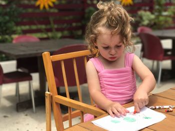 Cute girl making drawing on paper while sitting at outdoors cafe