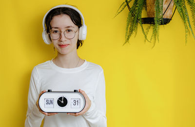 A teenage girl holds an alarm clock with the time, day and date