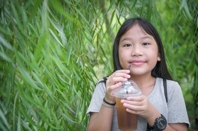 Portrait of smiling girl holding juice against plants