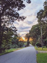 Empty road amidst trees against sky during sunset
