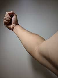 Cropped hand of man flexing muscles against white wall