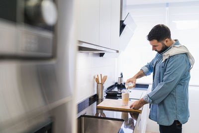 Man cooking in the kitchen in a denim shirt. a man is pouring milk into a container