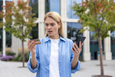 Portrait of young woman using mobile phone in city