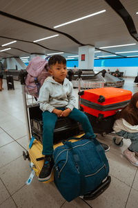 Portrait of woman sitting on suitcase at airport