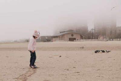 Young girl is playing on an empty beach during a foggy, cold day