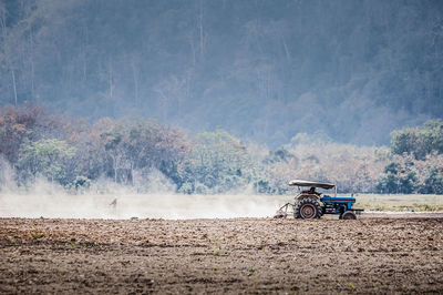 Tractor plowing field against trees