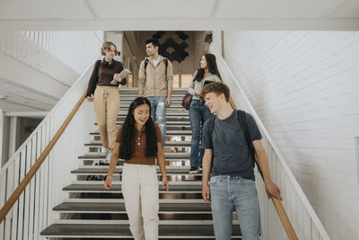 Happy multiracial male and female students moving down on steps in university