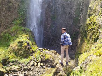 Full length of man standing on rock against waterfall