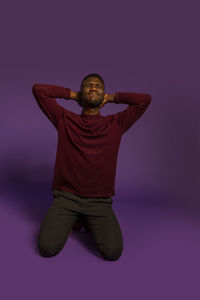 Portrait of young man standing against purple background