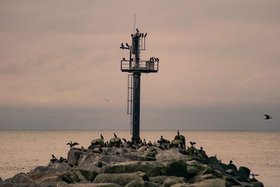 Cross on rock by sea against sky during sunset