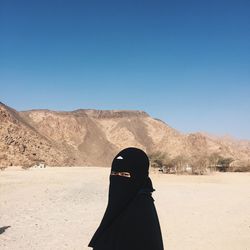 Portrait of woman in hijab standing on arid landscape against clear blue sky