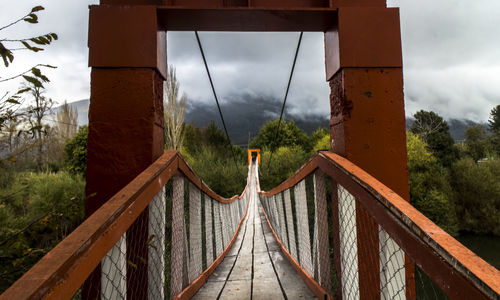 Footbridge amidst trees against sky
