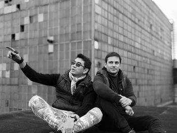 Man pointing while sitting with friend on building terrace 