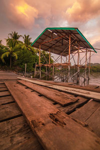 Wooden house by palm trees against sky during sunset