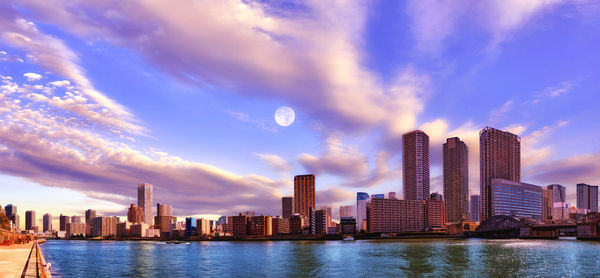 Sea by modern buildings against sky in city