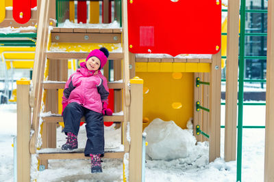 Happy girl sitting on outdoor play equipment during winter
