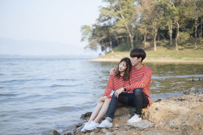 Young couple sitting on lake shore against forest