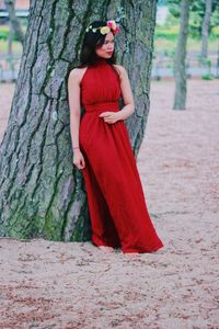 Woman in red dress standing against tree trunk