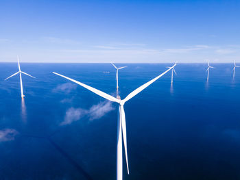 Wind turbines in sea against blue sky