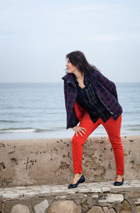 Young woman standing on retaining wall against sea