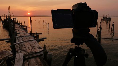 Man photographing on sea against sky during sunset