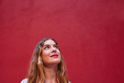 Headshot of a young blonde woman looking up to the side in front of a red wall. copy space.