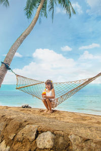 Girl drinking juice on hammock at beach