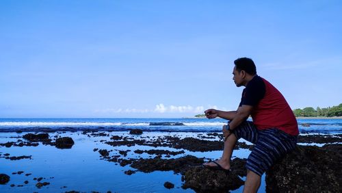 Side view of man standing at beach against clear sky