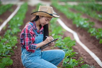 Woman using digital tablet while examining plants on agricultural field