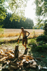 Full length of shirtless lumberjack standing by wood on field