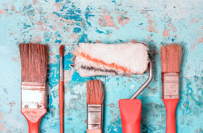 Set of painting brushes and rollers with red handles on a rustic wooden blue painted background.