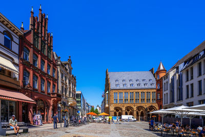 People on street amidst buildings in city against clear blue sky