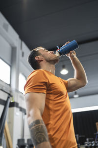 Thirsty man drinking water while standing in gym