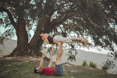 Young couple practicing acroyoga under oak tree