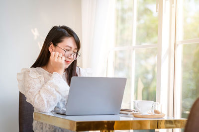 Young woman using phone while sitting on table