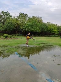 Father and son playing by pond against cloudy sky