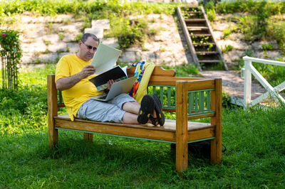 Mature man with laptop and documents working outside in garden, green home office concept.